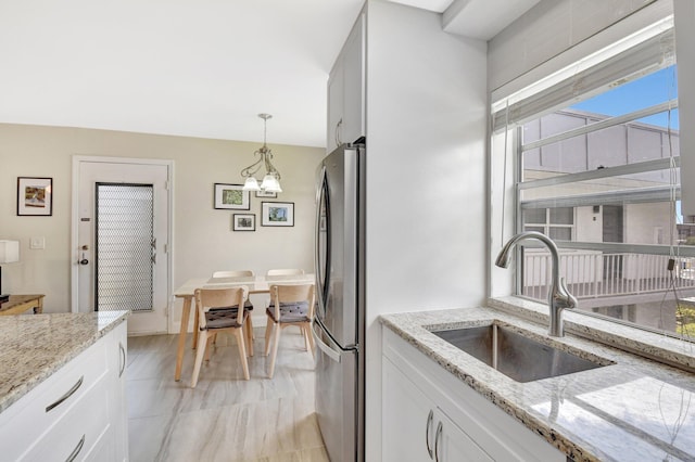 kitchen featuring a sink, freestanding refrigerator, decorative light fixtures, light stone countertops, and white cabinetry