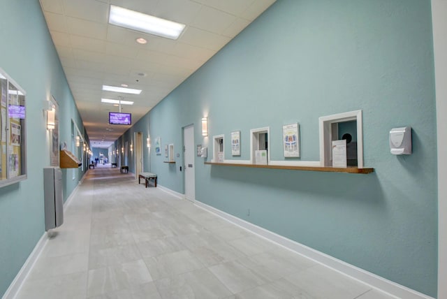 corridor with baseboards, a towering ceiling, and a paneled ceiling