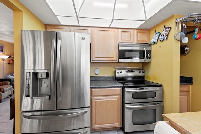 kitchen featuring dark countertops, light tile patterned flooring, light brown cabinetry, and stainless steel appliances