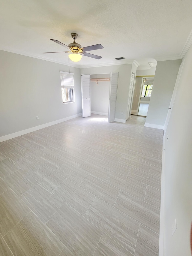 empty room featuring a wealth of natural light, visible vents, crown molding, and a ceiling fan
