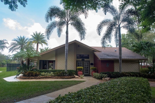 view of front facade featuring a front lawn, a shingled roof, stucco siding, and fence