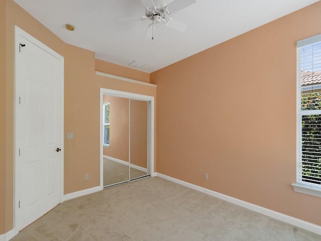 unfurnished bedroom featuring light colored carpet, baseboards, ceiling fan, and multiple windows