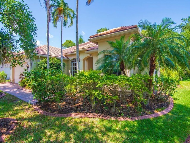 mediterranean / spanish-style house with an attached garage, stucco siding, a tiled roof, and a front yard