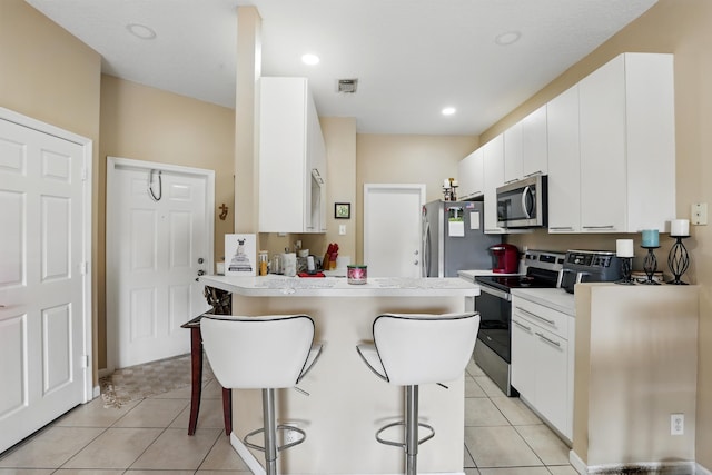 kitchen with white cabinets, a kitchen bar, stainless steel appliances, and light tile patterned floors