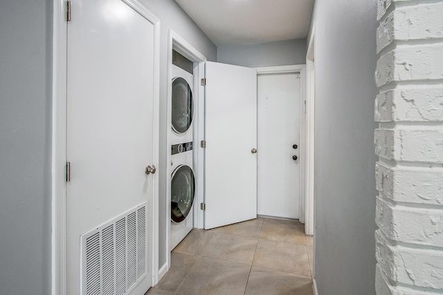 clothes washing area with laundry area, stacked washer / drying machine, visible vents, and light tile patterned floors