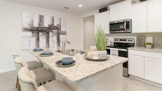 kitchen with stainless steel appliances, visible vents, light tile patterned floors, a sink, and white cabinetry