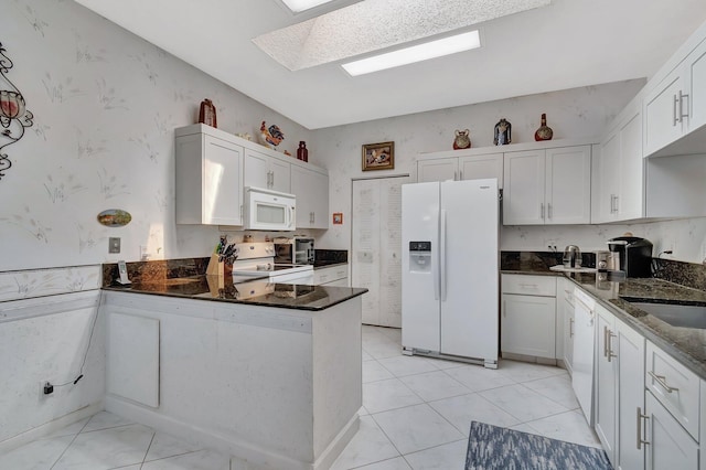7829 Mansfield Hollow Rd, Delray Beach, FL 33446 - kitchen with wallpapered walls, a skylight, white appliances, a peninsula, and white cabinetry
