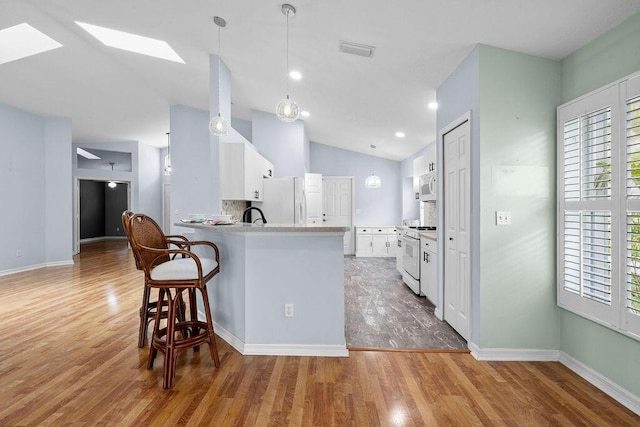 kitchen with white cabinetry, white appliances, a peninsula, and light wood finished floors