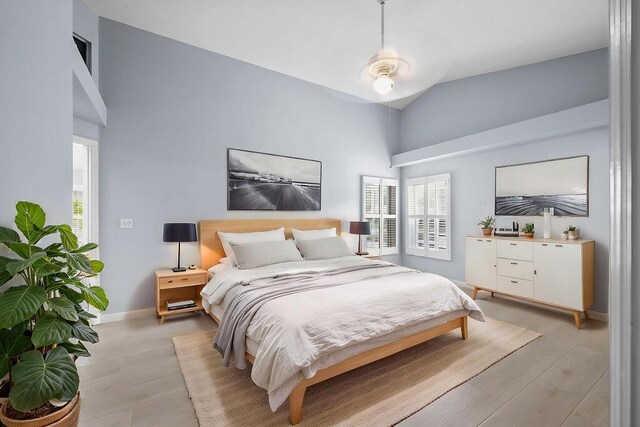 bedroom featuring multiple windows, baseboards, high vaulted ceiling, and light wood-style floors