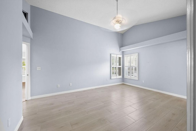 spare room with baseboards, high vaulted ceiling, wood finished floors, and a healthy amount of sunlight