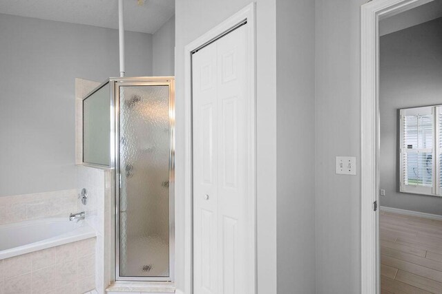 bathroom featuring a stall shower, a closet, a bath, and wood finished floors