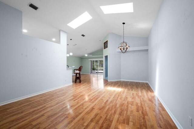 empty room with light wood finished floors, a notable chandelier, lofted ceiling with skylight, visible vents, and baseboards