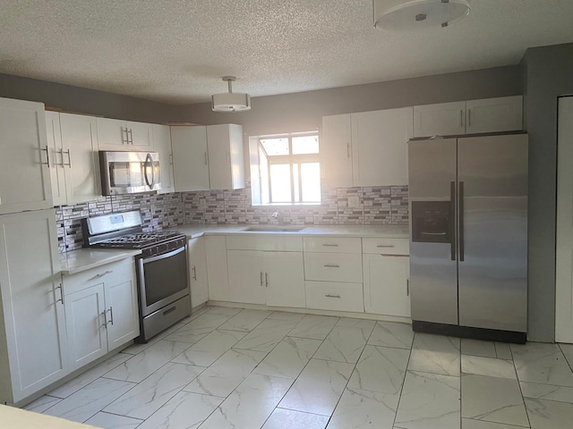 kitchen featuring white cabinets, a sink, marble finish floor, light countertops, and appliances with stainless steel finishes