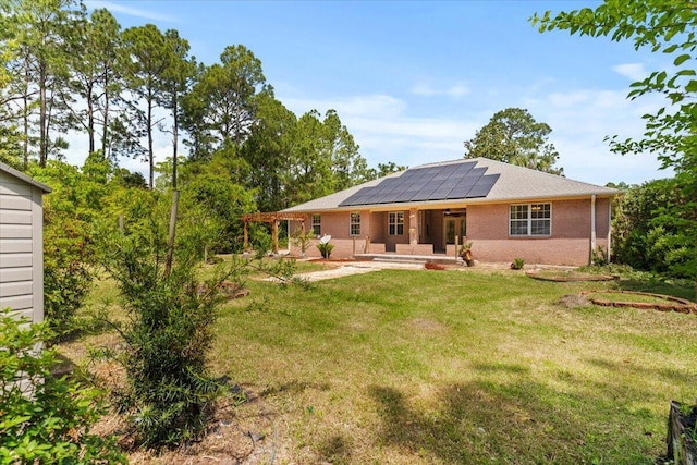 back of property with a yard, brick siding, a patio, and roof mounted solar panels