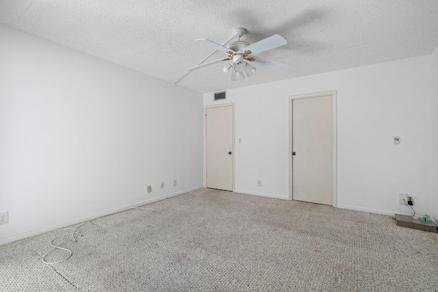 empty room featuring a textured ceiling, baseboards, visible vents, carpet, and a ceiling fan