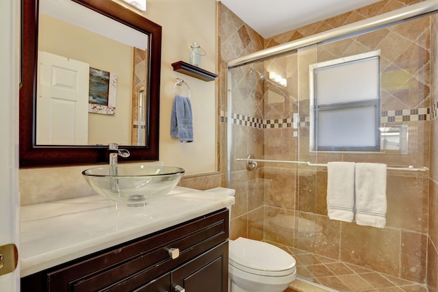 bathroom with toilet, tile walls, a shower stall, and vanity