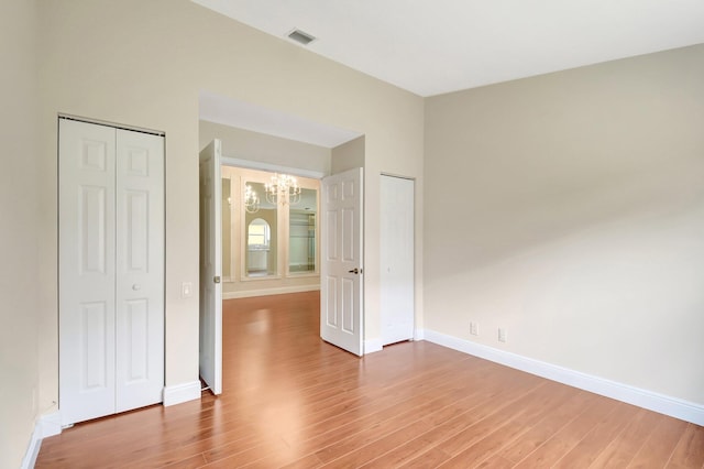 unfurnished bedroom with baseboards, an inviting chandelier, visible vents, and light wood-type flooring