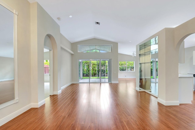 unfurnished living room with lofted ceiling, baseboards, wood finished floors, and arched walkways