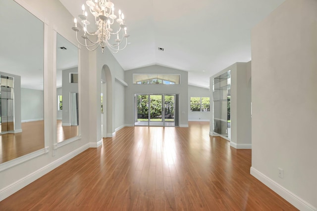 unfurnished living room featuring wood finished floors, a chandelier, arched walkways, baseboards, and lofted ceiling