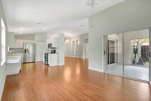 unfurnished living room featuring a sink, arched walkways, light wood finished floors, baseboards, and a notable chandelier
