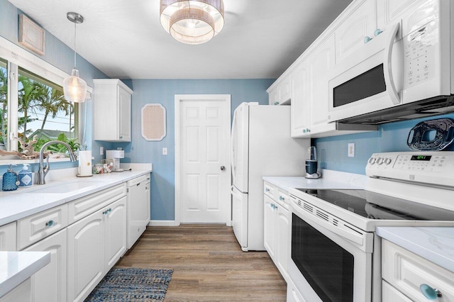 kitchen with pendant lighting, white appliances, a sink, wood finished floors, and white cabinets