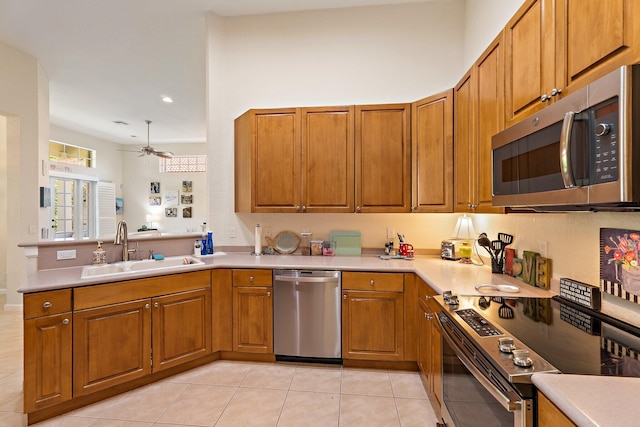 kitchen with a sink, a ceiling fan, appliances with stainless steel finishes, brown cabinets, and light tile patterned floors