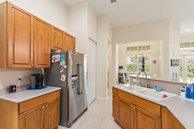 kitchen with a sink, light tile patterned flooring, high end fridge, brown cabinetry, and light countertops