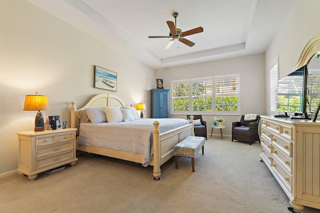 bedroom featuring light carpet, baseboards, a raised ceiling, and ceiling fan
