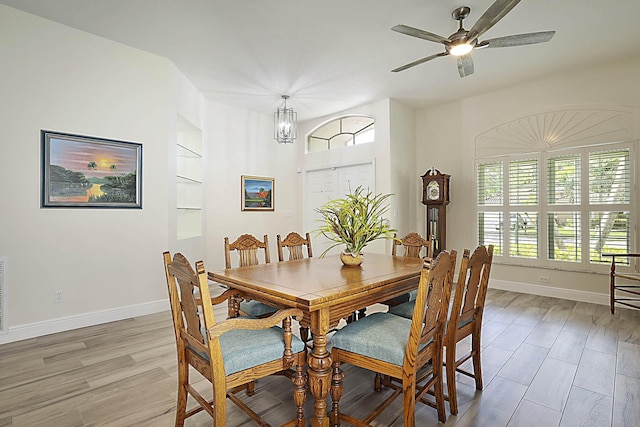 dining space featuring baseboards, light wood finished floors, ceiling fan with notable chandelier, and built in shelves