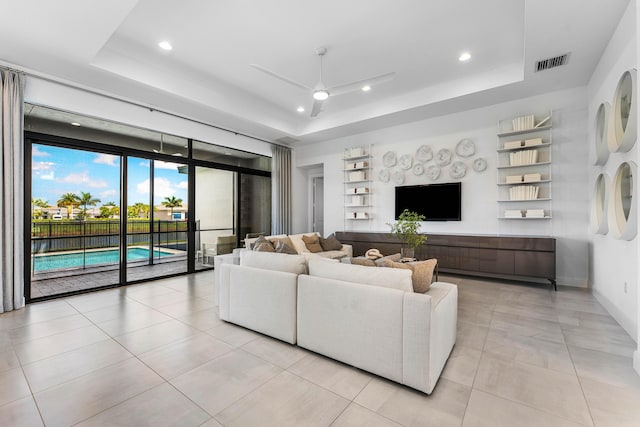 living area featuring a tray ceiling, a ceiling fan, recessed lighting, built in shelves, and light tile patterned floors