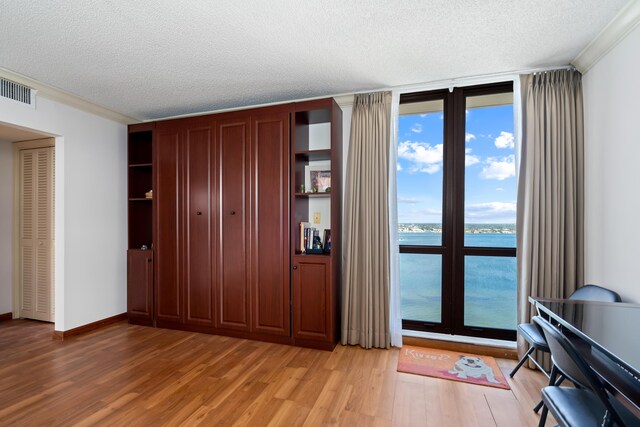 bedroom with crown molding, a textured ceiling, a water view, light wood finished floors, and visible vents