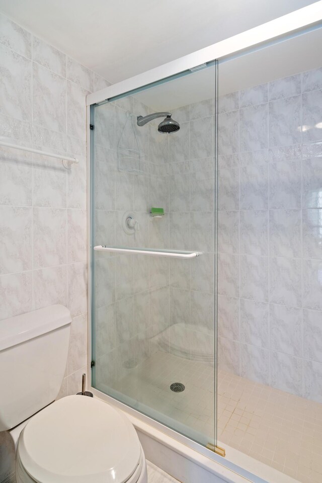 full bath with toilet, tile walls, and a stall shower