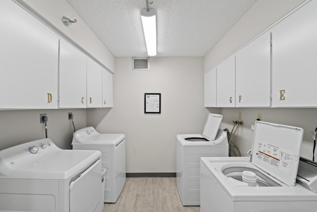 clothes washing area with visible vents, independent washer and dryer, light wood-style floors, cabinet space, and a textured ceiling