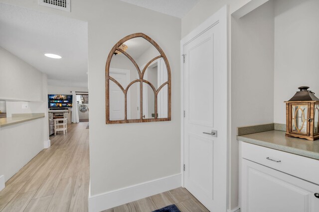 corridor with baseboards, light wood finished floors, and visible vents