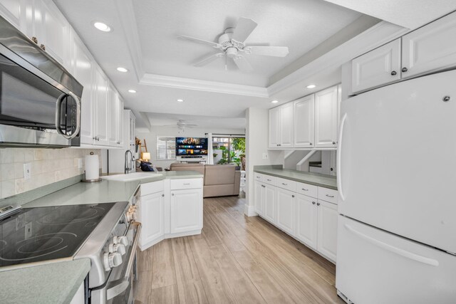 kitchen with ceiling fan, stainless steel appliances, a sink, open floor plan, and a tray ceiling