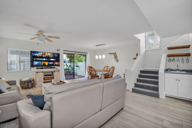 living room featuring light wood-style floors, stairs, ceiling fan, and indoor bar