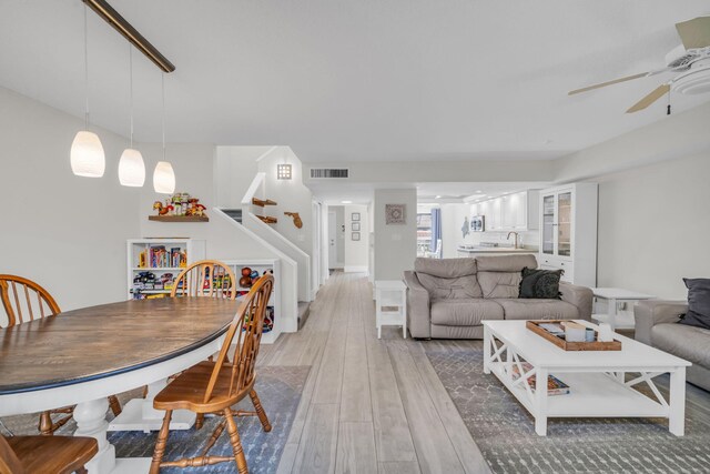 living area featuring visible vents, stairs, ceiling fan, and light wood finished floors