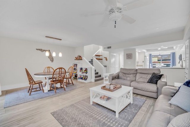 living room featuring light wood-style floors, ceiling fan, stairway, and visible vents