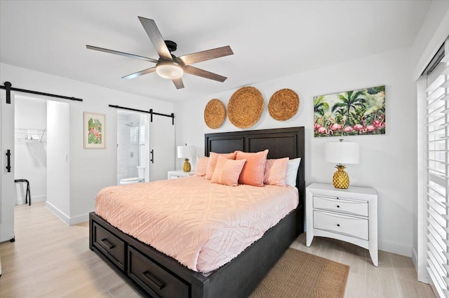 509 Oak Ter, Jupiter, FL 33458 - bedroom with a barn door, a ceiling fan, connected bathroom, light wood-type flooring, and baseboards