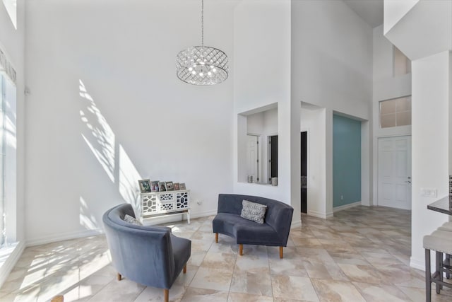 sitting room featuring a towering ceiling, a chandelier, a healthy amount of sunlight, and baseboards