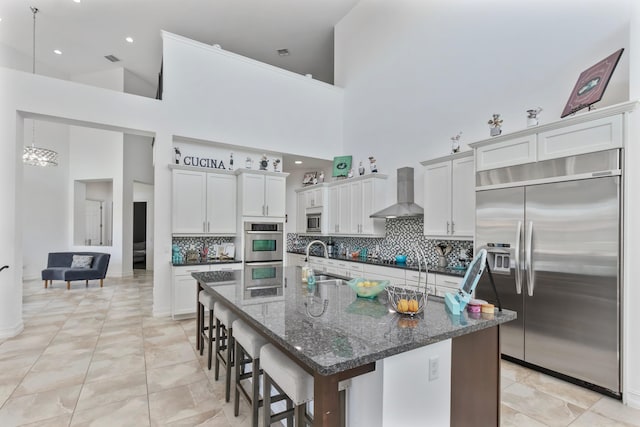 kitchen featuring built in appliances, wall chimney exhaust hood, a high ceiling, and a sink
