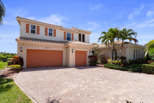 mediterranean / spanish-style house featuring a tile roof, decorative driveway, stucco siding, and a garage