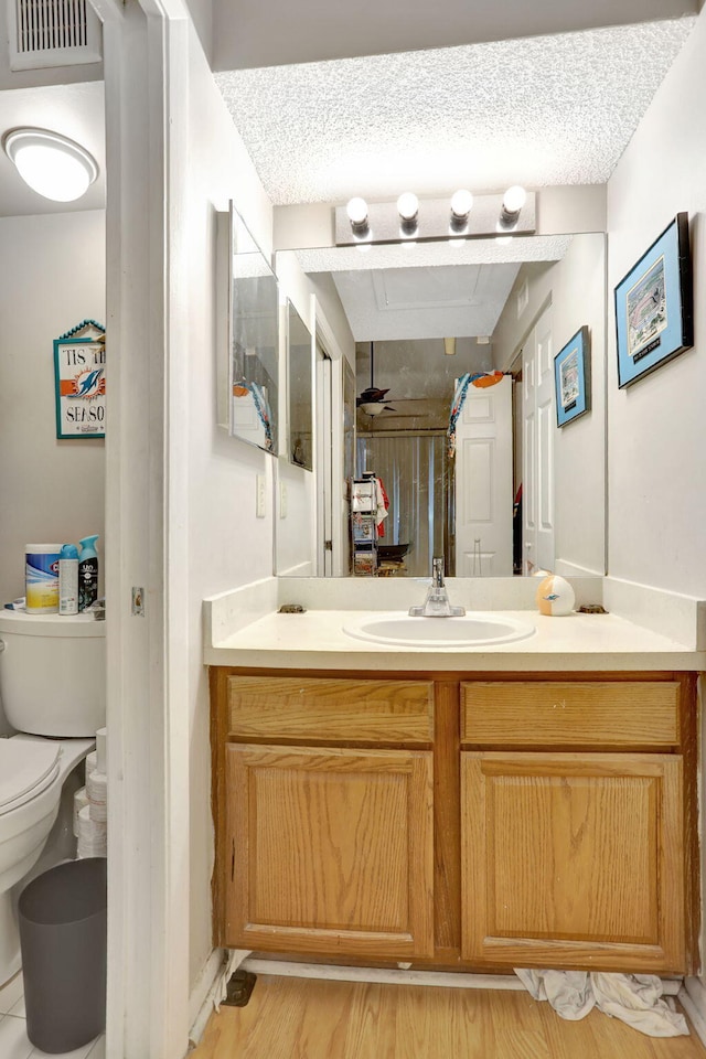 bathroom featuring vanity, toilet, a textured ceiling, wood finished floors, and visible vents