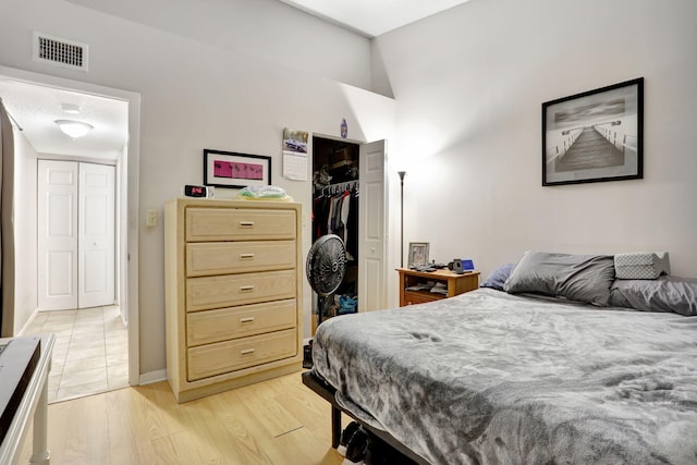bedroom with baseboards, visible vents, light wood finished floors, and a closet