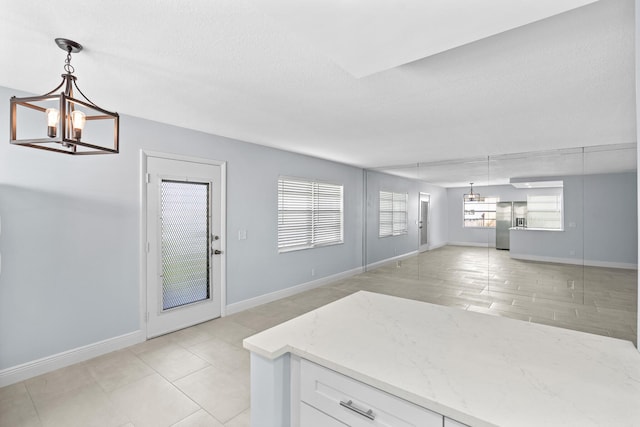 unfurnished living room with light tile patterned flooring, baseboards, and a notable chandelier