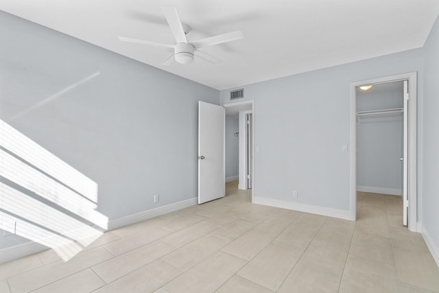 unfurnished bedroom featuring a spacious closet, visible vents, light tile patterned flooring, baseboards, and ceiling fan