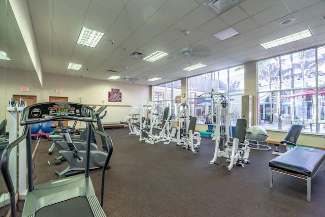exercise room featuring a ceiling fan, a paneled ceiling, and a healthy amount of sunlight