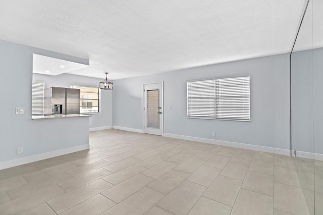 unfurnished living room featuring a chandelier, a textured ceiling, and baseboards