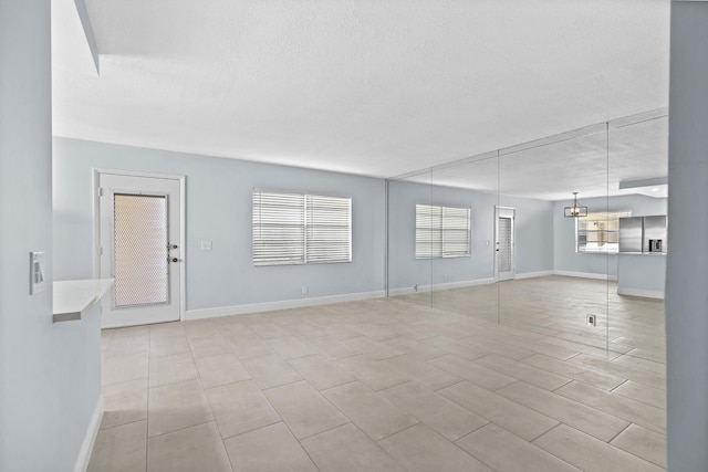 unfurnished living room with baseboards, a textured ceiling, and light tile patterned floors