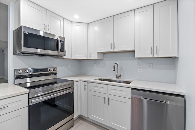 kitchen with light stone counters, white cabinetry, stainless steel appliances, and a sink